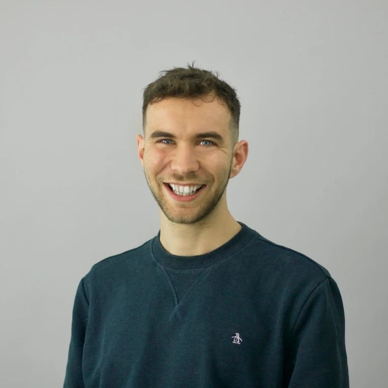 Tim Coysh, smiling, in a dark jumper against a plain grey background.